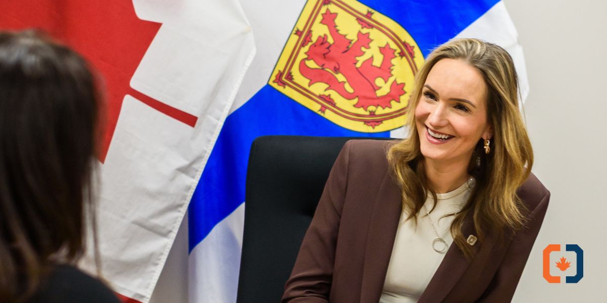 Rebecca Landry, CEO of Commissionaires Nova Scotia, smiles at unknown female while sitting in front of the Canadian and Nova Scotian flags at a board room table